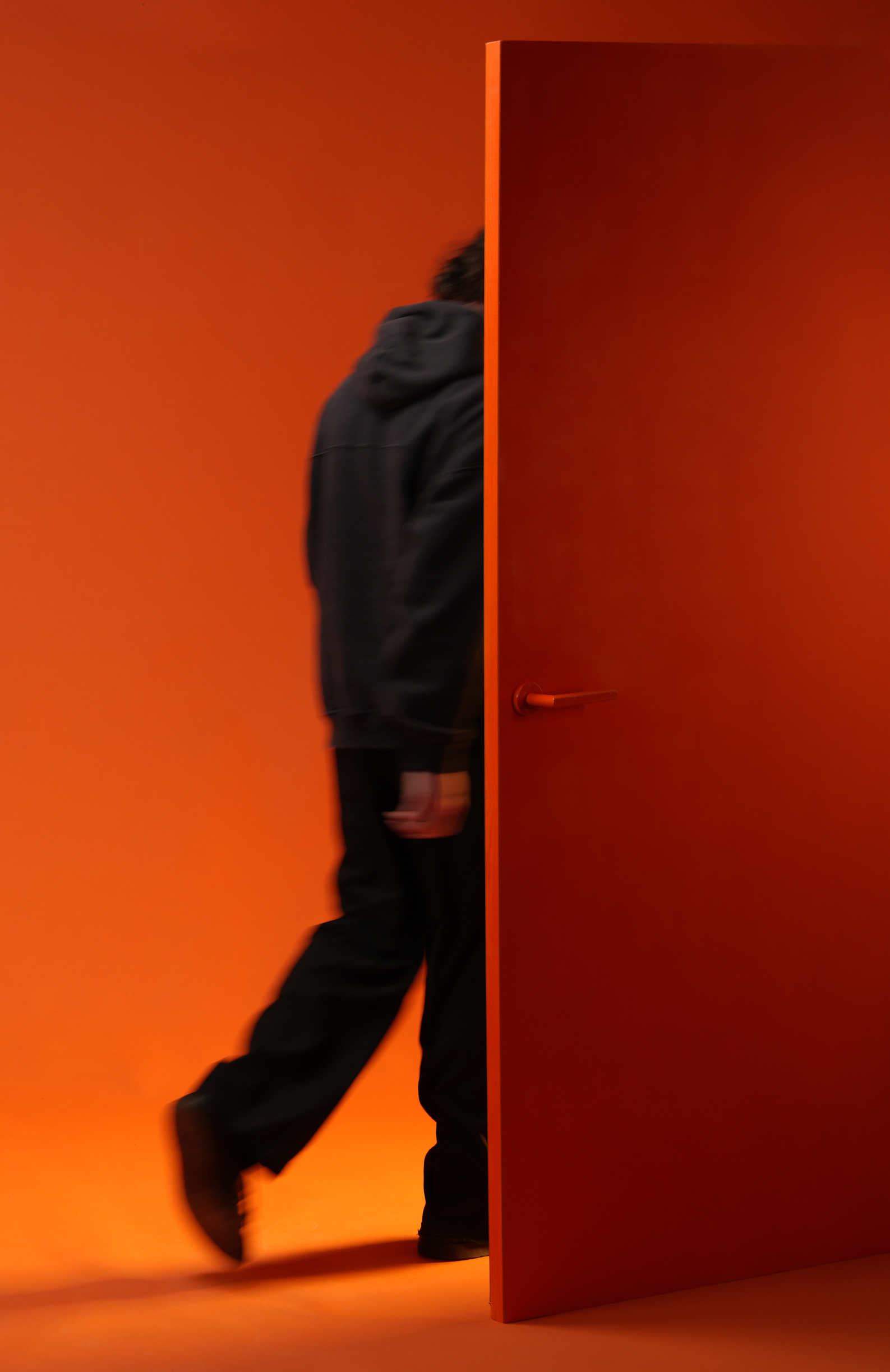 Person walking through a door with an orange backdrop