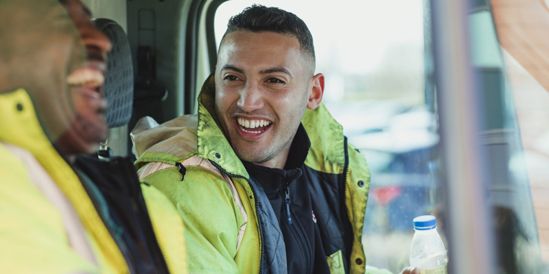 Two Male Labourers Talking And Laughing In Their Work Van Together Stock