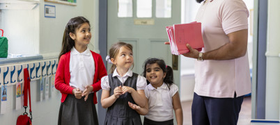 School teacher holding workbooks talking to school children