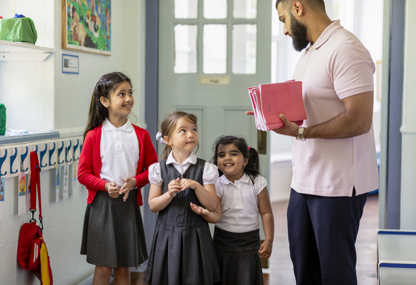 School teacher holding workbooks talking to school children