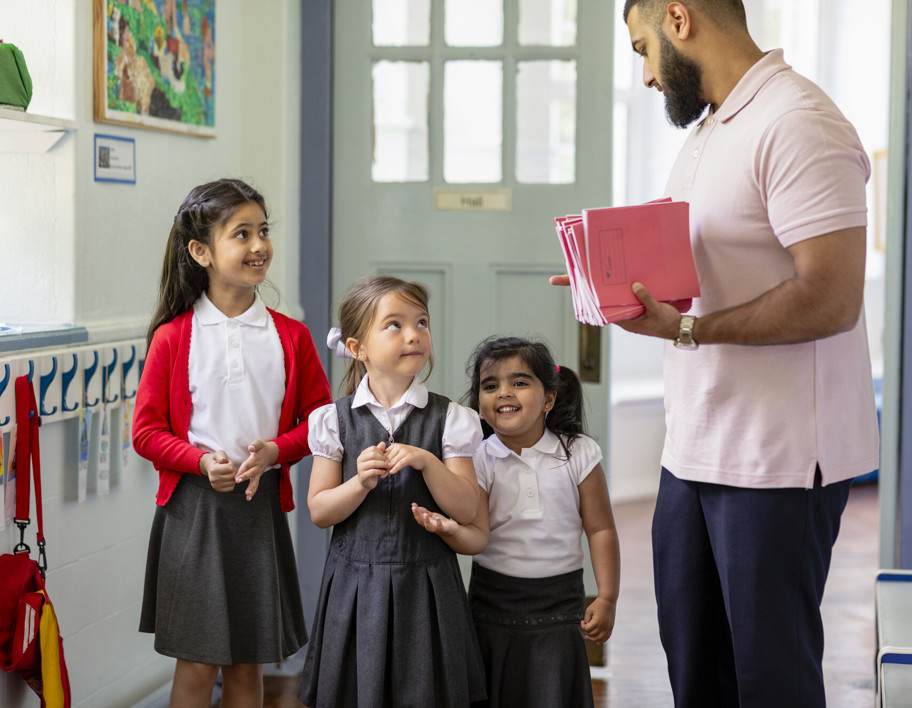 School teacher holding workbooks talking to school children