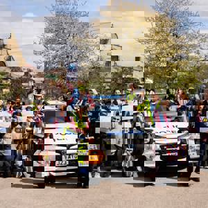 School children pose with police officers next to police car, holding hand-drawn road safety signs